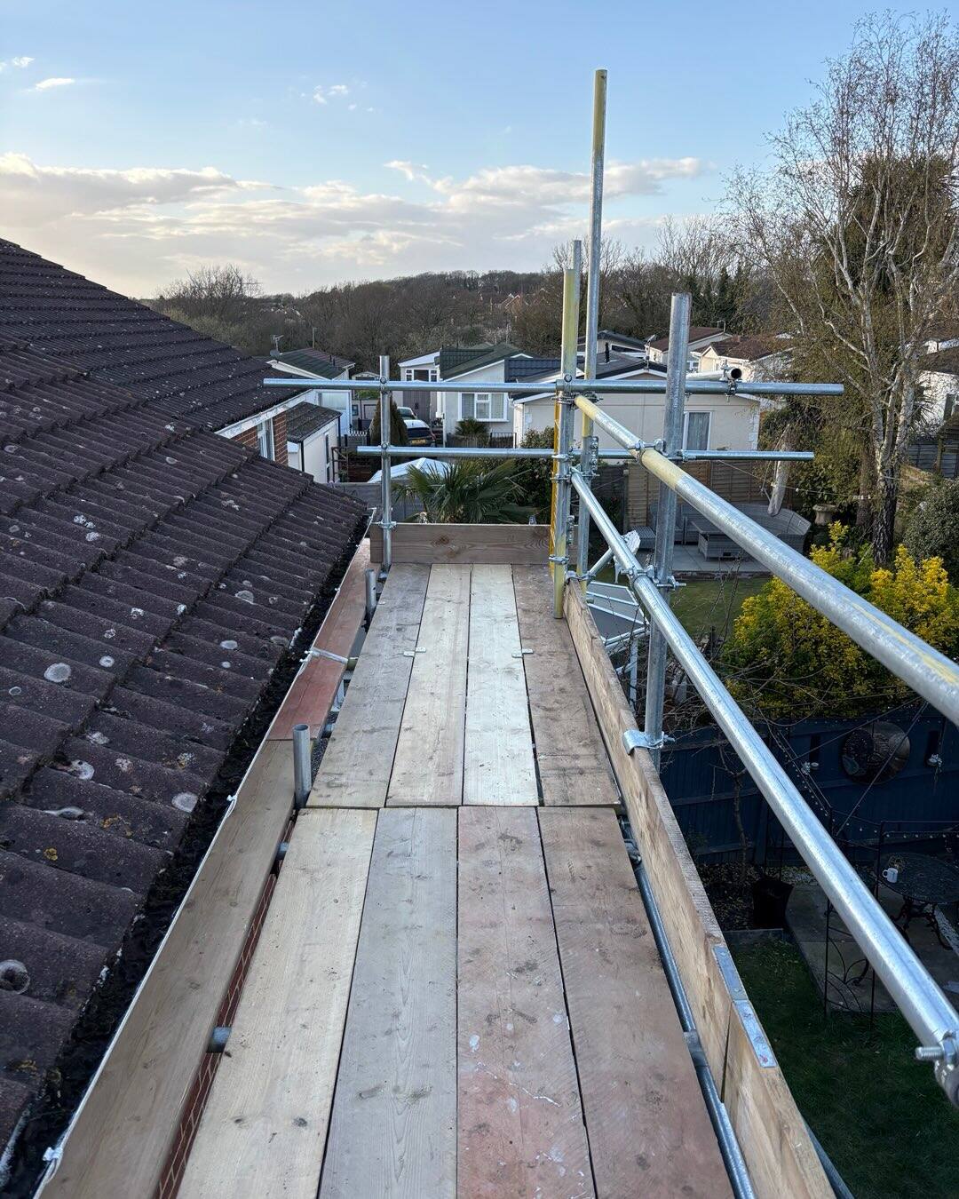 Scaffold deck along a bungalow roofline with gardens in the background