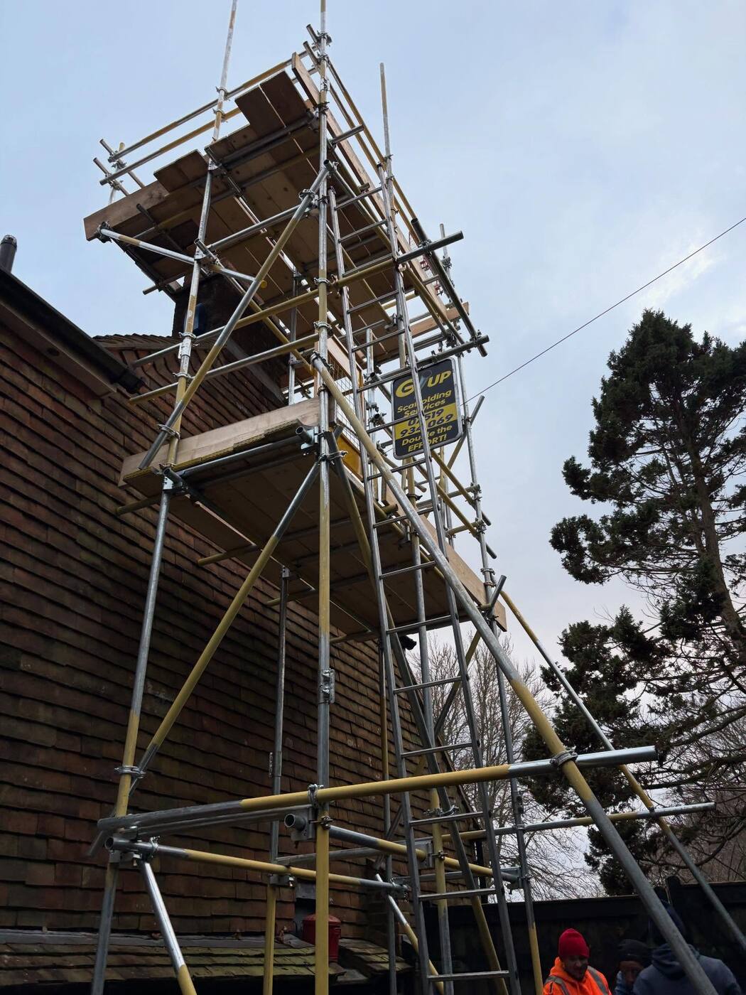 Tall standalone scaffold tower built up to a chimney stack with crew below