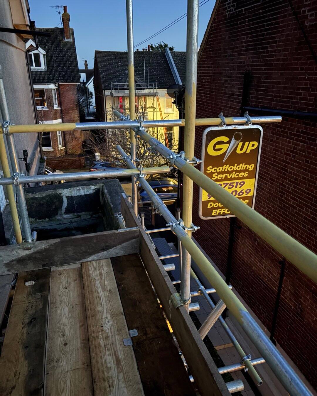 Golden hour shot of scaffold deck and G/UP sign against a brick wall